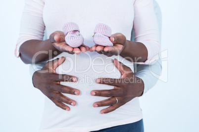 Pregnant woman holding baby shoes while husband touching her bel