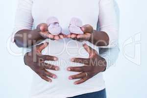 Pregnant woman holding baby shoes while husband touching her bel