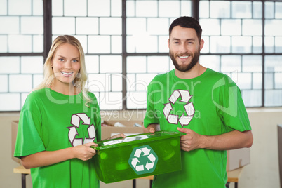 Portrait of smiling volunteers carrying recycling container