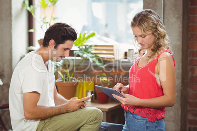 Woman with digital tablet while man using smartphone in office