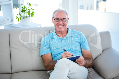 Happy senior man in eyeglasses sitting on sofa with clipboard