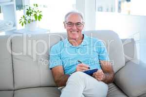 Happy senior man in eyeglasses sitting on sofa with clipboard