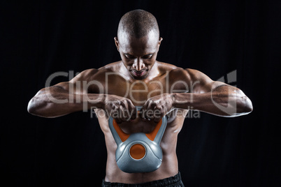 Muscular man looking down while exercising with kettlebell