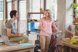 Woman standing with bicycle and discussing with colleague in off