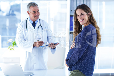 Portrait of smiling pregnant woman with male doctor in clinic