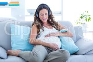 Happy pregnant woman listening music on sofa