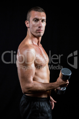 Portrait of confident shirtless athlete working out with dumbbel