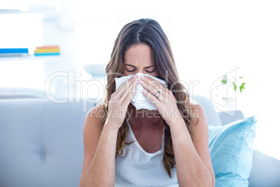 Sick woman sneezing on sofa