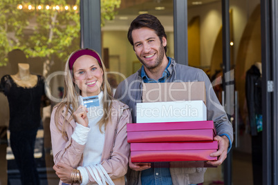 Smiling couple showing credit card and carrying boxes
