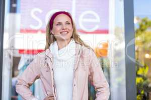 Smiling woman with hands on hips in front of sale sign