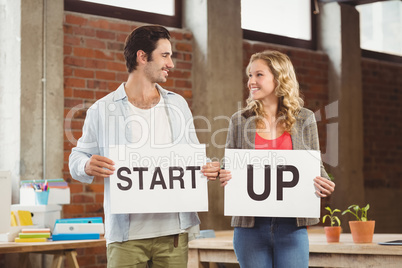 Smiling business people showing card with start up text in offic