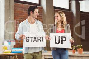 Smiling business people showing card with start up text in offic