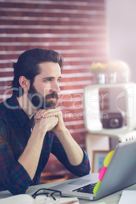 Thoughtful editor with hand clasped using laptop