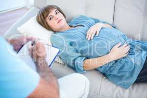 Pregnant woman holding belly while lying on sofa