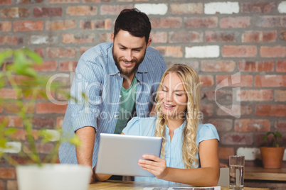 Cheerful businesswoman showing digital tablet to colleague