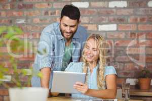 Cheerful businesswoman showing digital tablet to colleague