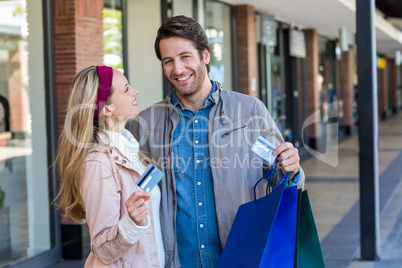 Smiling couple with shopping bags showing credit card