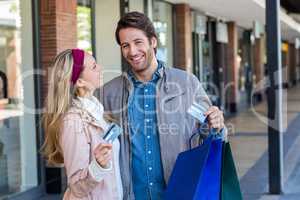 Smiling couple with shopping bags showing credit card