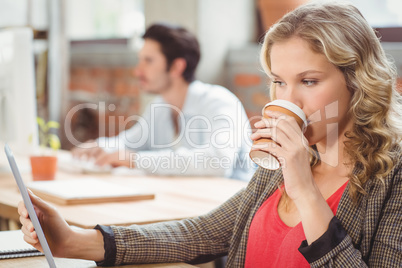 Woman drinking coffee while looking at digital tablet