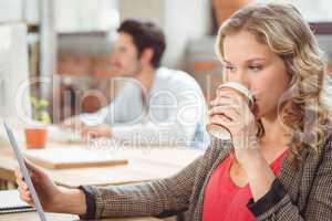 Woman drinking coffee while looking at digital tablet