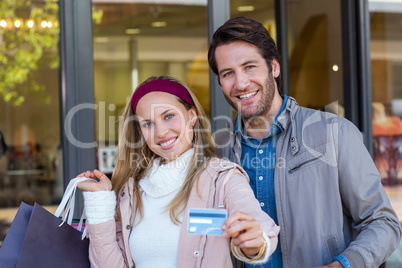 Smiling couple with shopping bags showing credit card
