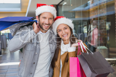 Young happy couple holding shopping bags with christmas hats on