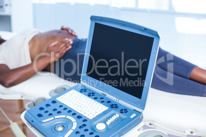 Ultrasound machine with pregnant woman lying in background