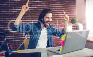 Happy creative businessman with arms raised looking at laptop