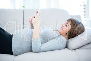 Smiling pregnant woman using smartphone while lying on sofa