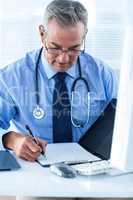 Male doctor writing data in file at hospital