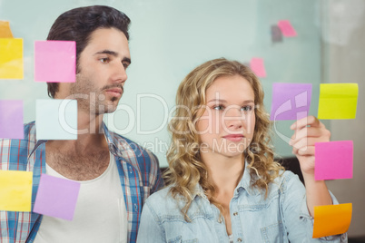 Man looking at woman sticking notes on glass