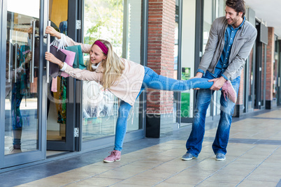Smiling man trying to pull away his girlfriend from clothes stor