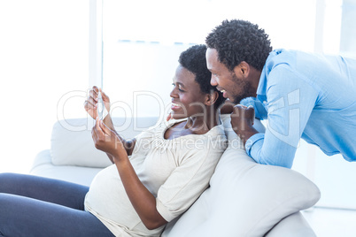 Pregnant woman showing photo to husband at home
