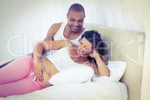 Happy pregnant wife with husband lying on bed