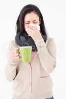 Sick woman blowing her nose while holding a green mug