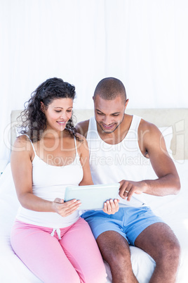 Husband with pregnant wife holding digital tablet