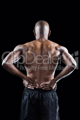 Rear view of muscular athlete stretching with hand on hip