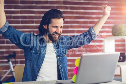 Smiling creative businessman with arms raised looking at laptop