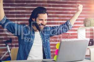 Smiling creative businessman with arms raised looking at laptop