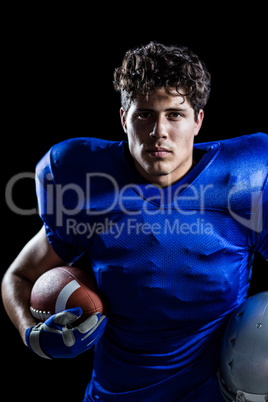 Portrait of serious American football player holding ball and he