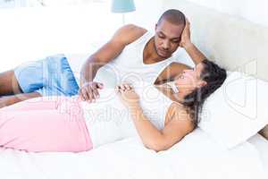 Happy pregnant wife relaxing with husband on bed