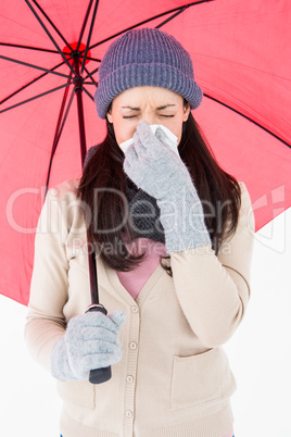 Sick brunette blowing her nose while holding an umbrella