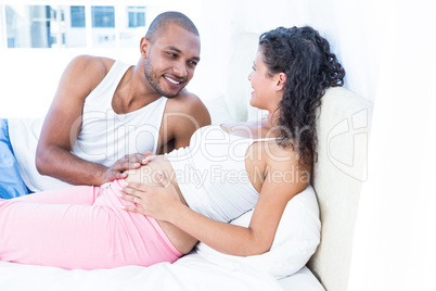 Happy husband lying with pregnant wife on bed