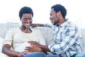 Happy man talking with pregnant wife touching her belly at home