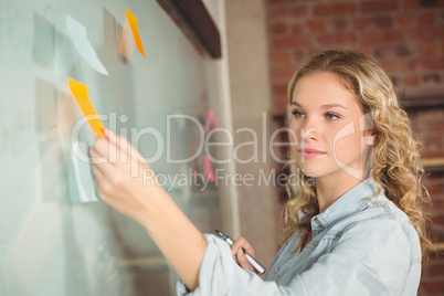 Beautiful businesswoman sticking notes on board in office