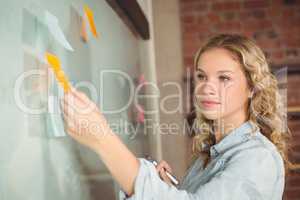 Beautiful businesswoman sticking notes on board in office