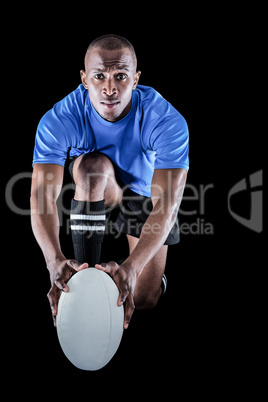 Portrait of rugby player kneeling and holding ball