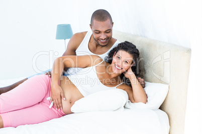 Portrait of pregnant woman with husband lying on bed