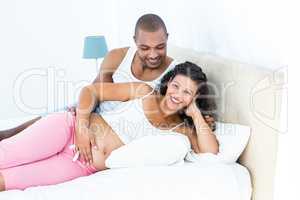 Portrait of pregnant woman with husband lying on bed