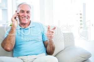 Senior happy man using smartphone while sitting on sofa